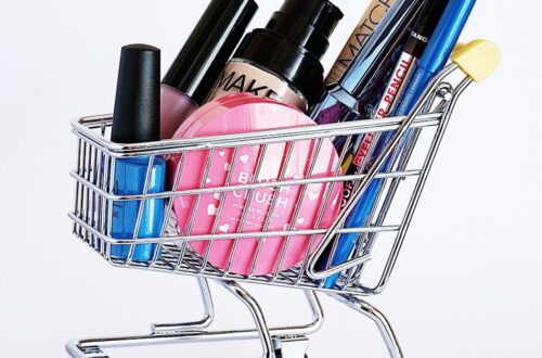 Miniature shopping cart filled with a variety of cosmetics on a white background.