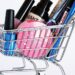 Miniature shopping cart filled with a variety of cosmetics on a white background.